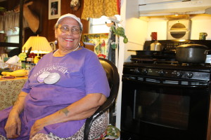 Joan Avant sits at her kitchen table at her home in Mashpee as a pot of her special dish, Three Sisters Rice, cooks on the stove.. She was making the stew for a group of volunteers who were helping her with repair jobs around her house as part of The Big Fix, a community service day organized by Housing Assistance Corporation.