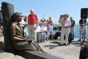 As the Reverend Deborah Warner of Church of the Messiah, Woods Hole gives a benediction, audience members admire sculptor David Lewis's statue of Rachel Carson at Waterfront Park in Woods Hole.