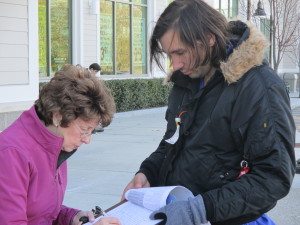 Loretta Bean of Plymouth signs a petition to get a candidate on the ballot.  Alex Arsenault of Somerville, on the right, is a professional petitioner.