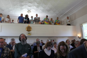 The congregation stands to sing a hymn before the baptism of Paul Rifkin at Waquoit Congregational Church. In the balcony, wearing tie dyed T-shirts are some staff from Rifkin's restaurant, Moonakis Cafe, who snuck away from work to attend the service.