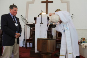 Paul Rifkin stands by the the Rev. Fields fills the batismal font with cold water for the baptism.
