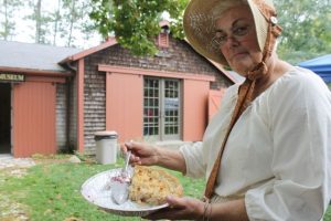 Pat Pisch, in period attire, shows off one of the prize-winning pies with the Stephen Dottridge House in the background.