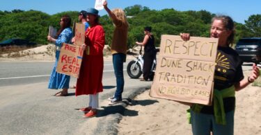 About a dozen people hold placards at an entrance to the Provincelands to protest the Cape Cod National Seashore decision to entertain bids for 10-year leases on some dune shacks. CAPE COD WAVE PHOTO