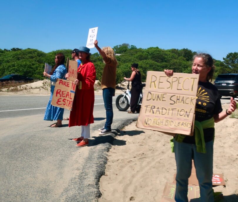 About a dozen people hold placards at an entrance to the Provincelands to protest the Cape Cod National Seashore decision to entertain bids for 10-year leases on some dune shacks. CAPE COD WAVE PHOTO